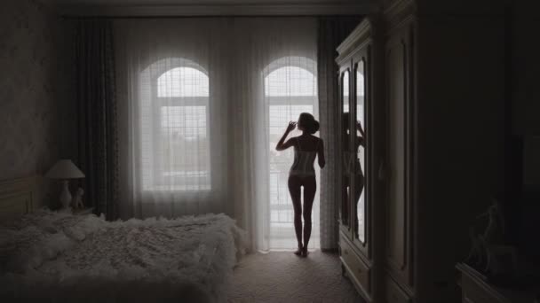 Silhouet van een mooi slank meisje bij het raam in de slaapkamer — Stockvideo