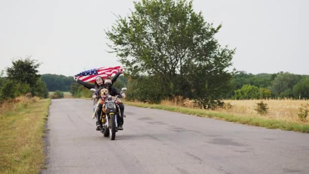 Пара байкеров с собакой на мотоцикле с флагом Америки — стоковое видео