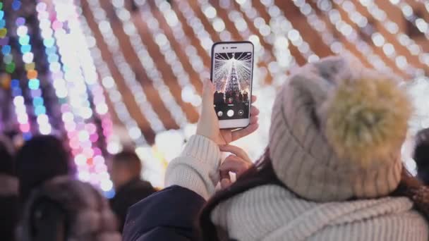 Una mujer fotografía un árbol de Navidad de la ciudad en su teléfono inteligente — Vídeo de stock