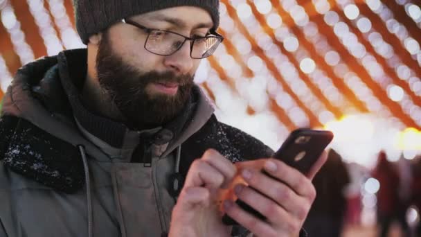 Бородатий Людиною Окулярах Використовувати Смартфон App Різдвяні Вогні Snowy Вечір — стокове відео