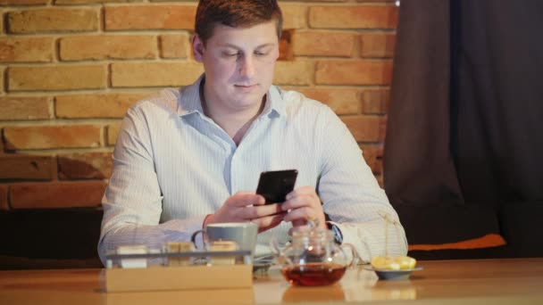 魅力的な男性の肖像画は カフェで使用電話を座っています レンガの壁のバーでスマート フォンで座っているハンサムな男 — ストック動画