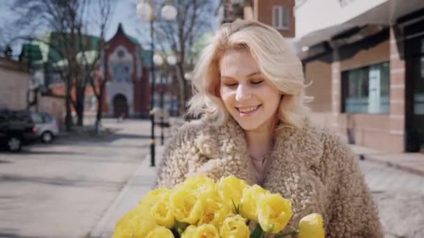 Щаслива дівчина гуляє з букетом жовтих тюльпанів вздовж вулиці — стокове відео