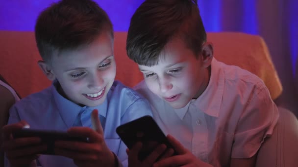 Два симпатичных мальчика играют в видеоигры со смартфоном в помещении — стоковое видео