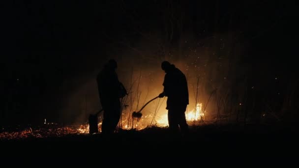 Twee brandweerlieden met vuur flappers Blus een brand in de nacht — Stockvideo