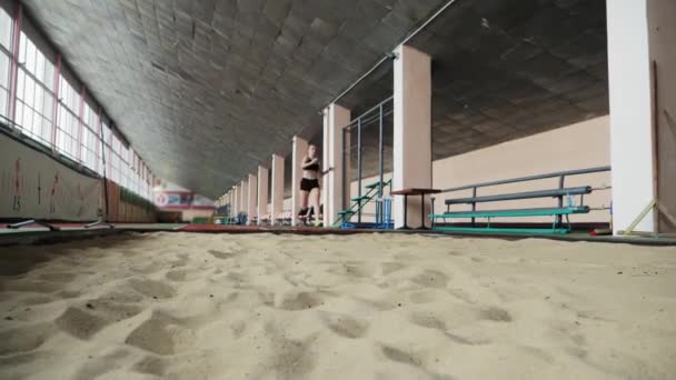 Flicka idrottsman utför långa hoppa in i sandlådan inomhus — Stockvideo