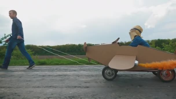 Vater rollt Sohn in selbstgebasteltem Pappflugzeug — Stockvideo