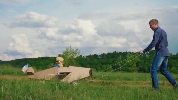 Ein kleiner Junge fährt mit einem selbstgebastelten Pappflugzeug. Konzept der freundlichen Familie — Stockvideo