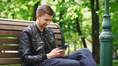 Parkta bir bankta otururken akıllı telefon kullanan çekici adam