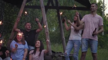 Genç arkadaşlar grubu bir kamp ateşi etrafında şarkı söylüyor