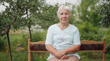 Yaşlı kadın bahçede bir bankta oturan