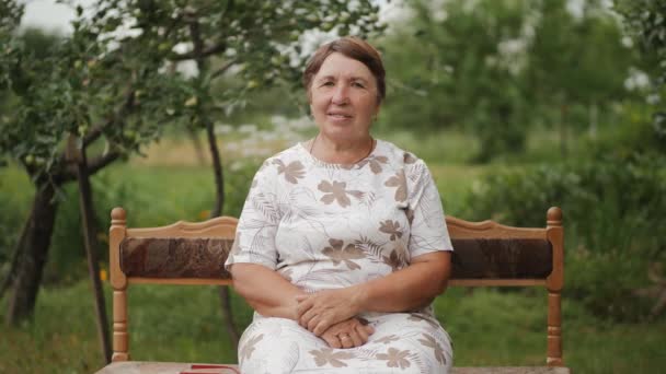 Oudere vrouw zittend op een bankje in de tuin — Stockvideo