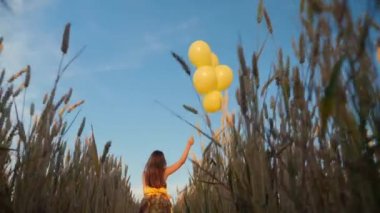 Genç kız buğday tarlasında balonlarla koşuyor