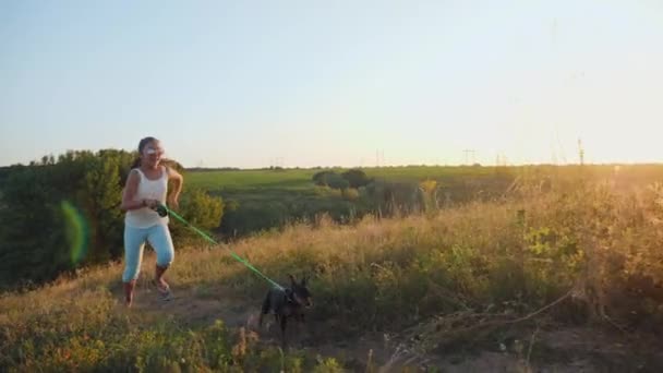 Chica corre con un perro con una correa en una zona montañosa — Vídeos de Stock