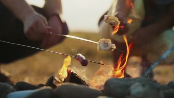 La gente fríe tocino y salchichas en brochetas en una hoguera — Vídeos de Stock