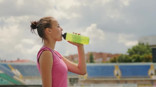 Девушка-спортсмен пьет воду на стадионе — стоковое видео