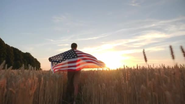 El hombre camina con la bandera de América en el campo — Vídeos de Stock