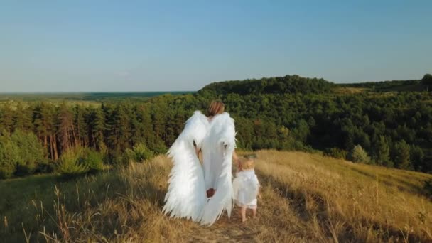 一个带着孩子的女孩打扮成天使在大自然中行走 — 图库视频影像