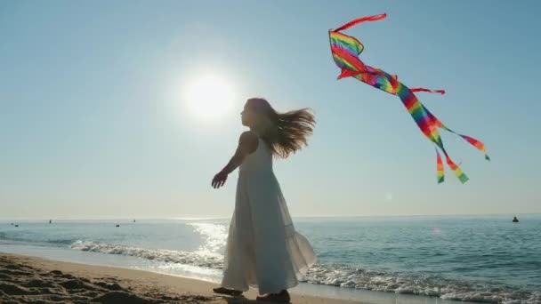 Chica en un vestido blanco juega con una cometa en la orilla del mar — Vídeos de Stock