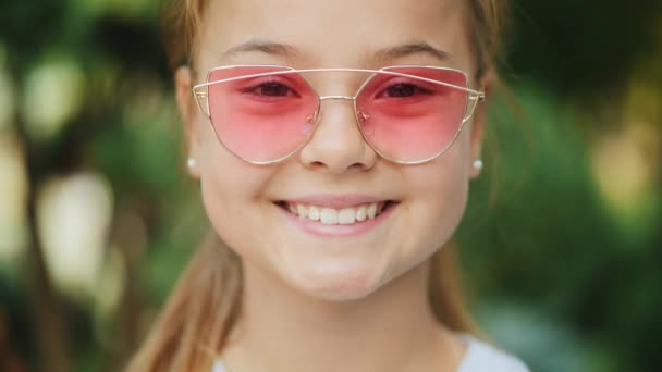 Pembe güneş gözlüğü açık havada genç gülümseyen kız, closeup — Stok video