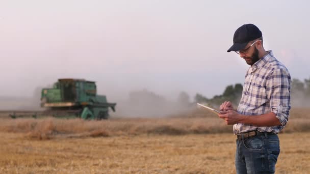 Farmer utiliza una tableta digital en el fondo de una combinación de trabajo — Vídeo de stock