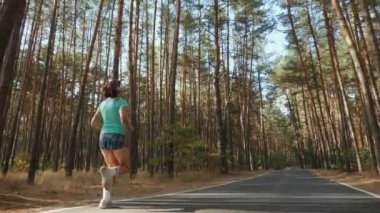 Atletik kız bir çam ormanında yol boyunca çalışır