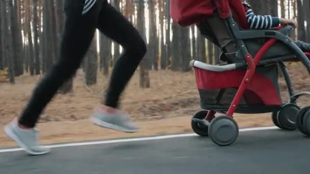 Uma mulher a correr com um carrinho de bebé. Só as pernas fecham. — Vídeo de Stock