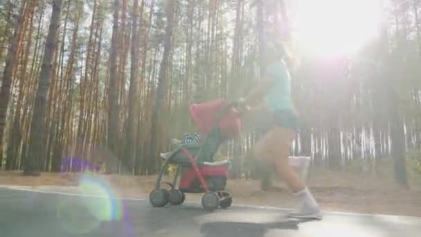 Correndo mulher com carrinho de bebê na estrada na floresta — Vídeo de Stock