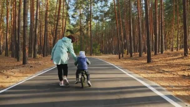 ママは、道路上のバランスバイクに乗るために小さな息子を教えます — ストック動画