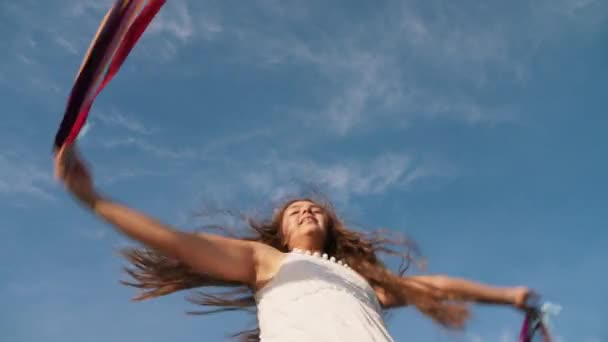 Chica joven gira, juega con cintas de colores al aire libre — Vídeos de Stock