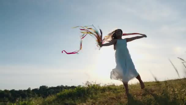 Meisje met regenboog linten loopt naar de top van de heuvel — Stockvideo