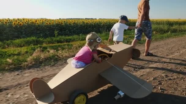 Papa und sein kleiner Sohn rollen Pappflugzeug mit einem Mädchen — Stockvideo