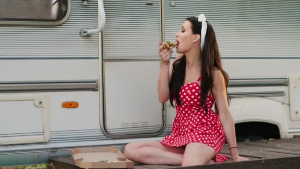 Chica comiendo un pedazo de pizza mientras se sienta cerca de la caravana — Vídeo de stock