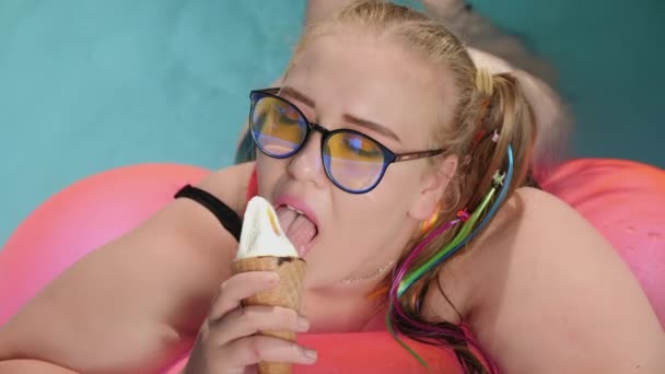 Толстая девушка ест мороженое во время купания в бассейне — стоковое видео