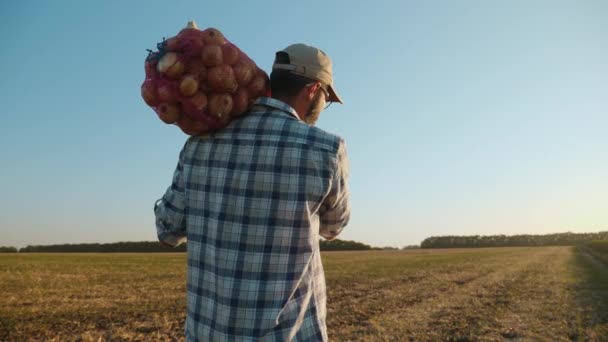 Un granjero lleva una bolsa de cebollas en su hombro — Vídeos de Stock