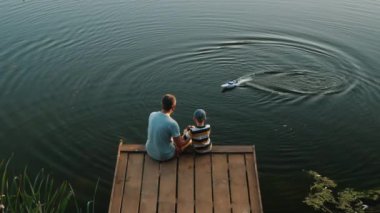 Baba ve küçük oğlu gölde oyuncak sürat teknesiyle oynuyorlar.