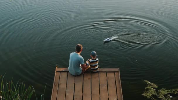 Tata i mały syn bawią się motorówką RC na jeziorze — Wideo stockowe