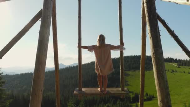 Uma mulher balançando na frente de uma grande vista sobre as montanhas — Vídeo de Stock