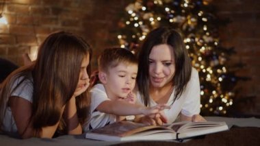 Anne ve çocuklar yatakta uzanıp birlikte kitap okuyorlar.