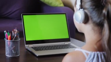 Liseli kız yeşil ekranlı bir dizüstü bilgisayara bakıyor.