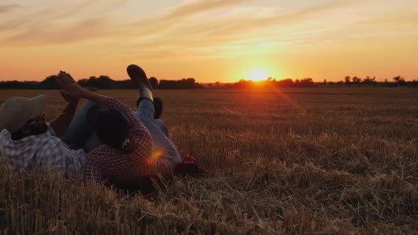 Pareja de granjeros descansando sobre paja en un campo al atardecer — Vídeos de Stock