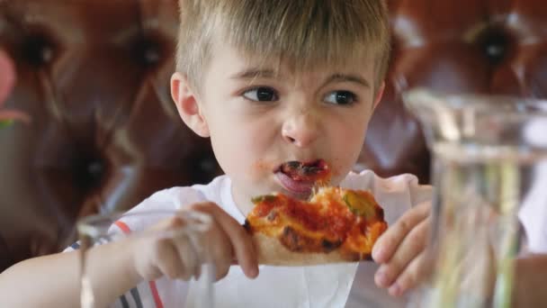 Mały chłopiec w kawiarni fast food je pizzę. — Wideo stockowe