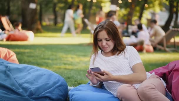 Девушка пользуется смартфоном в городском парке — стоковое видео