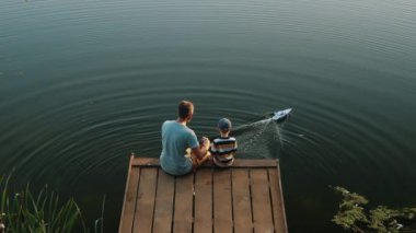Baba ve küçük oğlu gölde oyuncak sürat teknesiyle oynuyorlar.