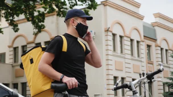 O homem de entrega em uma máscara protetora fala em um celular — Vídeo de Stock