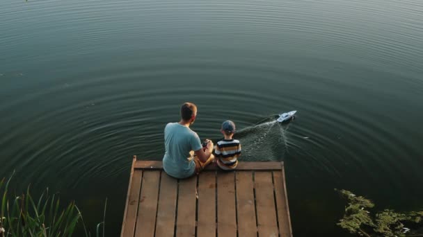 Батько і маленький син грають з RC іграшковим швидкісним човном на озері — стокове відео