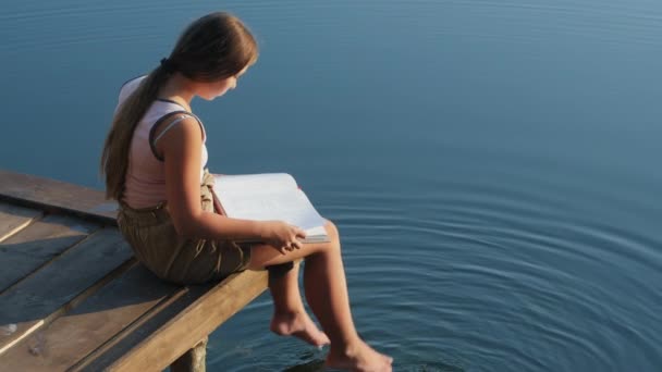 Une jeune fille lisant un livre sur le lac — Video