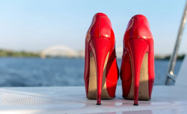 Pair of used  red high heel women shoes on yacht desk. Close up view.