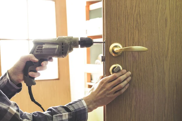 Carpenter repairs, installs a lock in a wooden door spinning the screw with a drill.