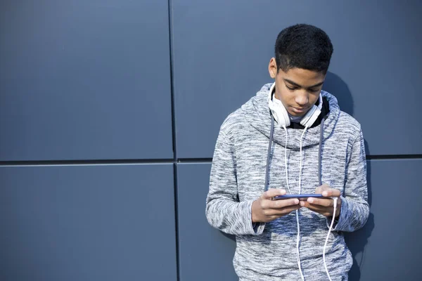 young man in headphones listening to music on a smartphone. African American guy playing a game on a mobile phone.