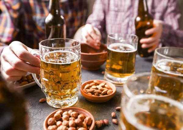 A group of friends are drinking beer from mugs in a bar at the table.